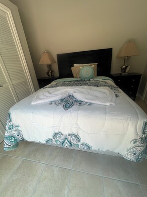 A neatly made bed with a patterned bedspread, two bedside tables with lamps, and a closed door.