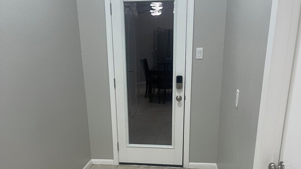 A hallway with a white door, a dining area in the background, and a tiled floor.