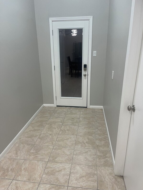 A hallway with a white door, a dining area in the background, and a tiled floor.