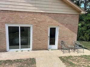 A brick building with two large sliding glass doors, a patio area with a metal chair, and a small table.