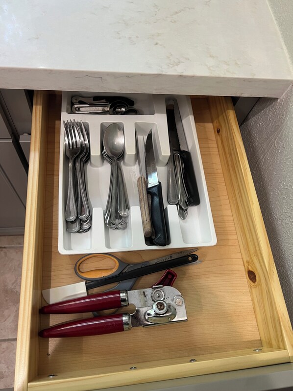 A drawer containing a knife, spoon, fork, and other utensils.