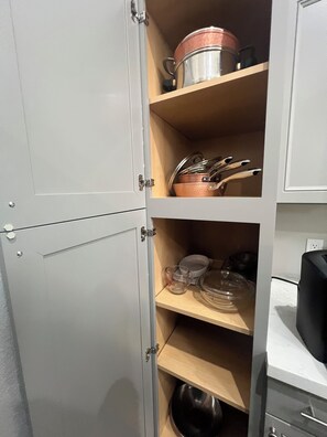 Un meuble de cuisine doté d’étagères où sont rangés des ustensiles de cuisine, une bouilloire et une machine à café.