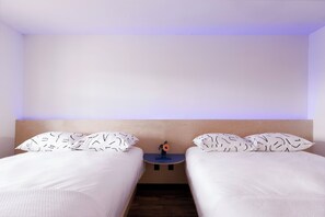 A hotel room with two beds, a small table with a vase, and a plain wall. - The Iris Motel - Queen Room (Nashville)