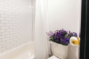 A bathroom with white tiled walls, a white bathtub, and a shower curtain.