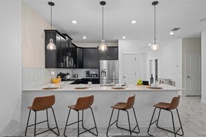 A modern kitchen with dark cabinets, stainless steel appliances, and pendant lighting. - 9BR Sleeps 26 - Private Pool & Spa Near Disney (Kissimmee)