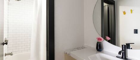 A modern bathroom with a white bathtub, a large mirror, and a sink with a black faucet.