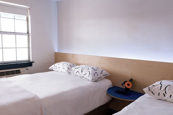 A bedroom with a bed, a nightstand, a window, and a wall-mounted heater.
