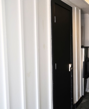 A closed black door with a silver handle, white walls, and a black floor. - The Iris Motel - Queen Room (Nashville)