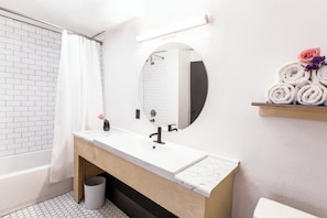A modern bathroom with a white sink, wooden vanity, a round mirror, and a towel rack with rolled towels.
