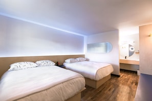 Moderni hotellihuone, jossa on kaksi sänkyä, suuri peili, puulattia sekä kylpyhuone, jossa on pesuallas ja peili.
