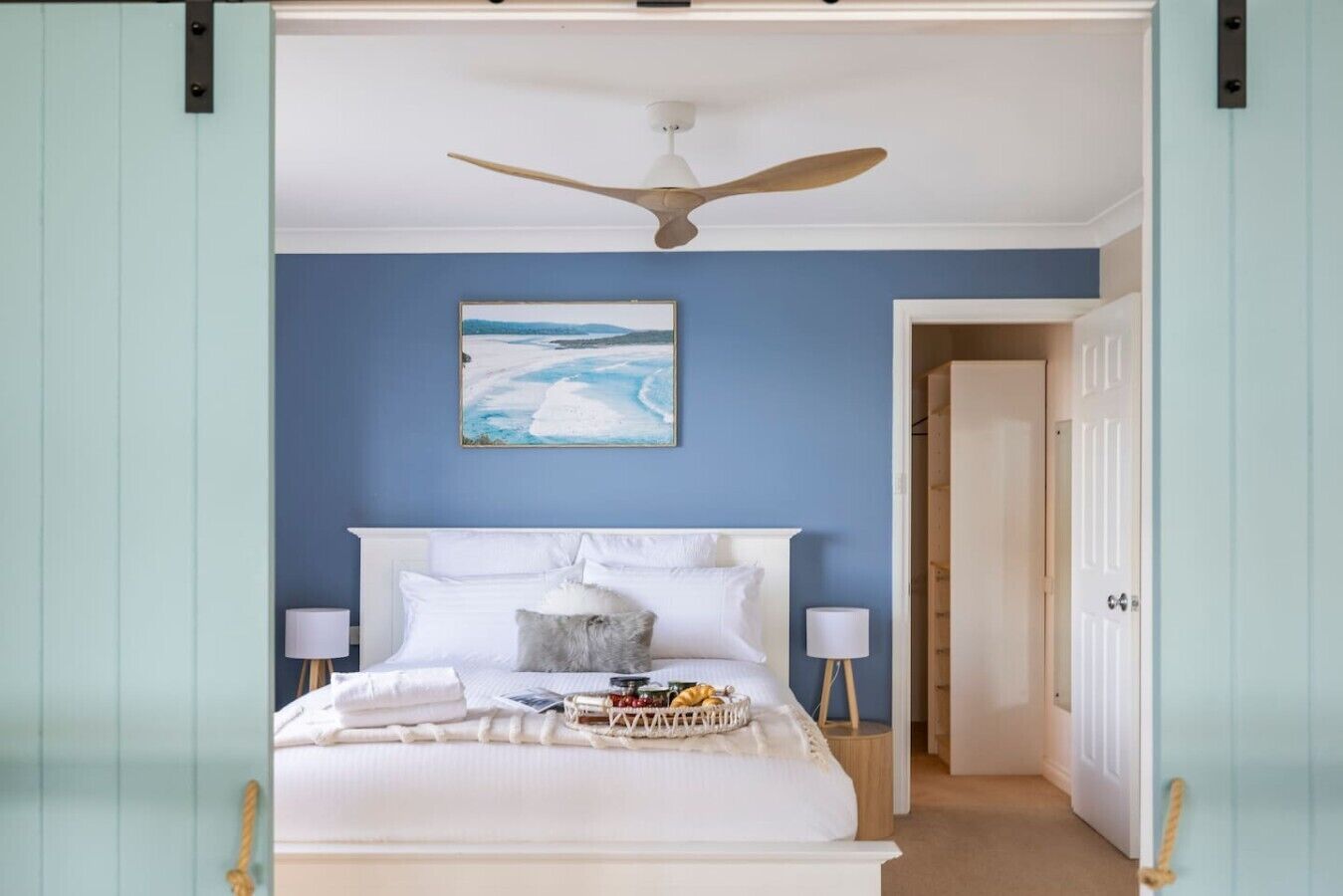 Een slaapkamer met een bed, een plafondventilator, bedlampjes, een ingelijste foto aan de muur en een deur die naar een andere kamer leidt.