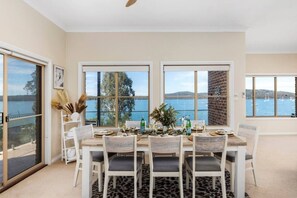 Comedor con una mesa para cuatro, ventanas amplias con vista al mar y una pared de ladrillo.