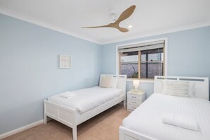 Ein Schlafzimmer mit zwei Einzelbetten, einem Deckenventilator, einem Fenster mit Jalousien und einem Nachttisch mit Lampe.