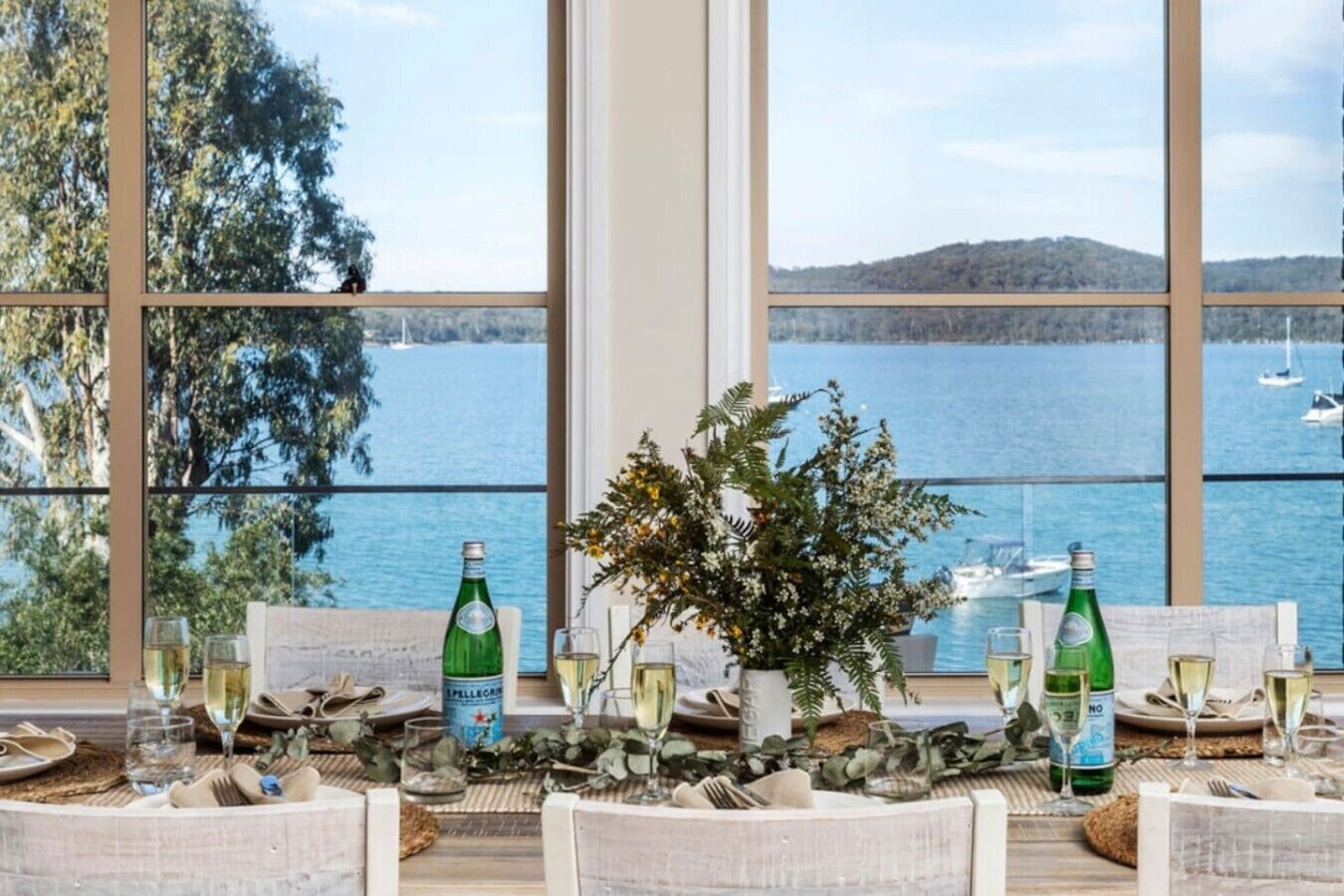 A table set for dining with a view of a lake and boats, bottles of Spillecar, and a potted plant.