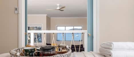 Une chambre à coucher avec un lit, un panier contenant divers objets, un magazine et une vue sur la mer par la fenêtre.