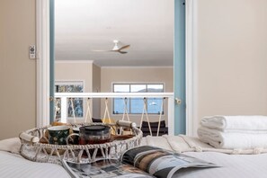 Ein Schlafzimmer mit einem Bett, einem Korb voller Gegenstände, einer Zeitschrift und Meerblick durch ein Fenster.