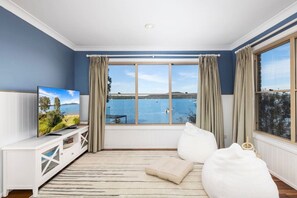 Una habitación con un ventanal grande, televisión, sofá blanco y vista al mar.