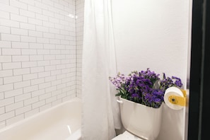 Un baño con paredes de azulejos blancos, una bañera blanca y un cortinero de ducha.