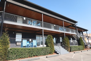 Un edificio de dos pisos con balcón, escaleras y estacionamiento.