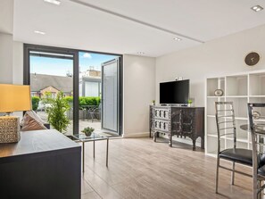 Ein modernes Wohnzimmer mit einem Flachbildfernseher, einem Essbereich mit rundem Tisch und Stühlen und einer großen Schiebeglasdoor, die auf einen Balkon führt.