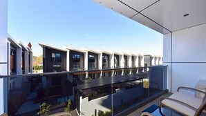 A modern balcony with glass railings, wicker furniture, and a view of adjacent buildings. - Elegant City Retreat with Balcony (Christchurch)