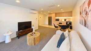 A modern living room with a flat-screen TV, a sofa, a coffee table, and a dining area with chairs. - Elegant City Retreat with Balcony (Christchurch)