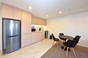 A modern kitchen with a stainless steel refrigerator, a microwave, and a stove. There is a dining area with a round table and four chairs. - Elegant City Retreat with Balcony (Christchurch)