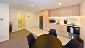 A modern kitchen with a dining area, featuring a refrigerator, microwave, stove, and a sink. - Elegant City Retreat with Balcony (Christchurch)
