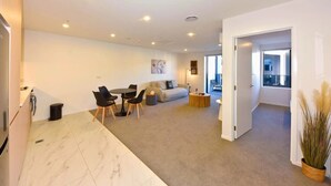 A modern living room with a sofa, coffee table, and dining area. - Elegant City Retreat with Balcony (Christchurch)