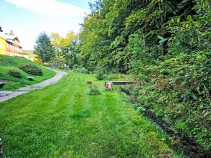 A well-maintained grassy area with a pathway leading to a building, surrounded by dense foliage. - Vacation home Sára by Interhome (Janské Lázně)