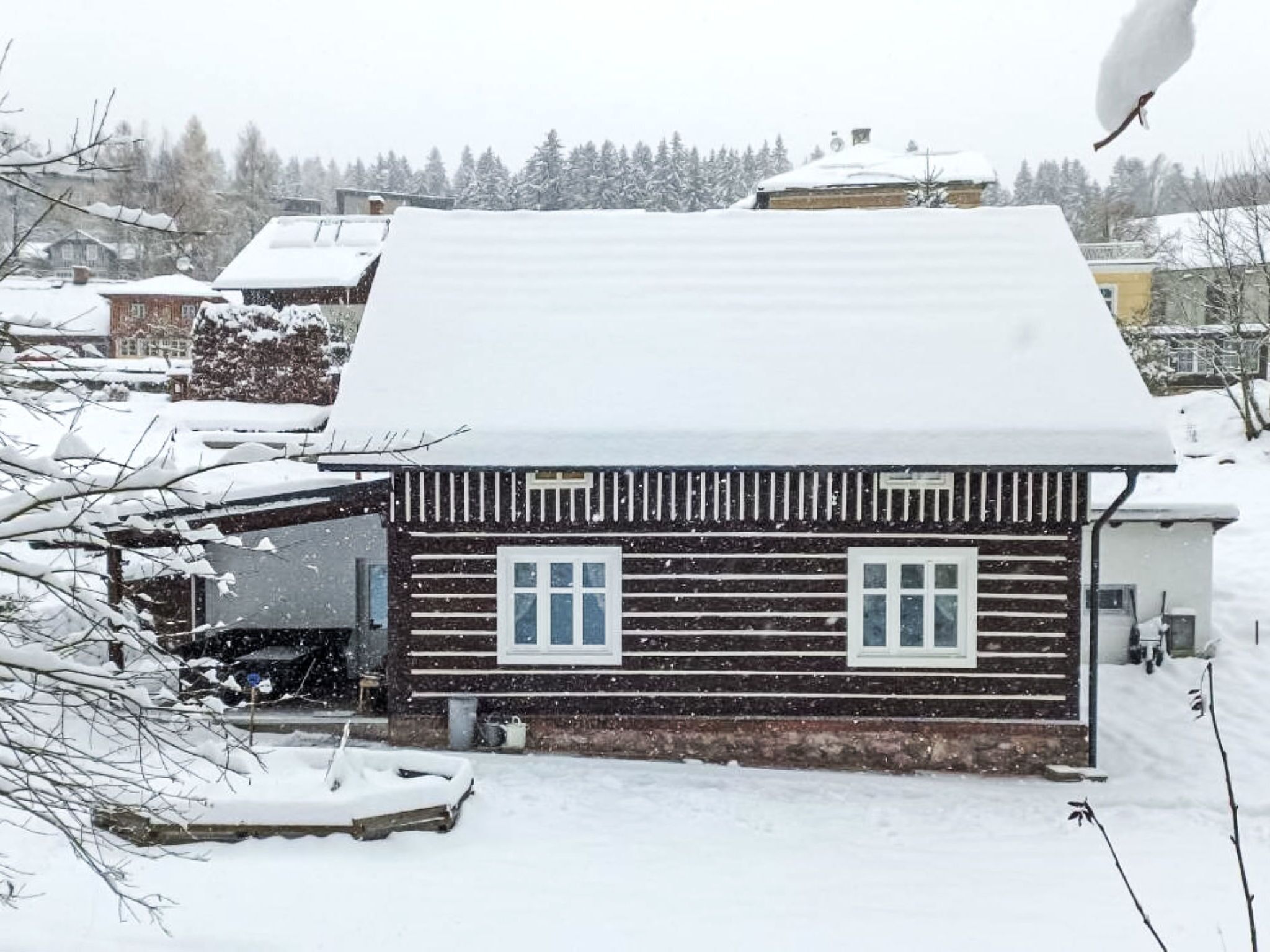 A wooden cabin with a snow-covered roof, a visible garage door, and a small porch area.