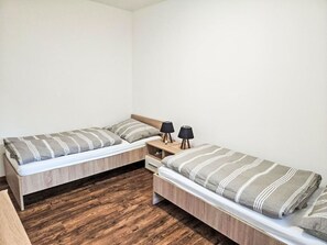 Un petit logement composé d’une seule pièce, avec deux lits, un plancher en bois et une table de chevet dotée de deux lampes.