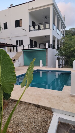Un edificio moderno su due piani con piscina, patio coperto e garage con persiane verdi.