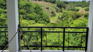 Ein Balkon mit einer Tauschaukel, weißen Säulen und Blick auf eine grüne Landschaft.