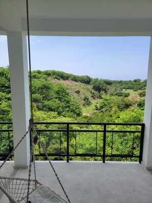 Ein Balkon mit einer Tauschaukel, weißen Säulen und Blick auf eine grüne Landschaft.