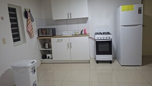 Cozinha compacta com armários brancos, micro-ondas, fogão a gás e geladeira.