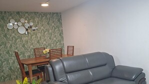 Um sofá de couro cinzento, uma mesa de jantar com cadeiras e uma parede decorativa com padrões de folhas.