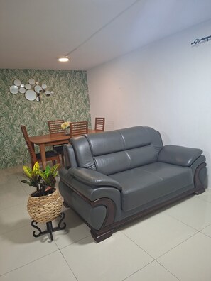 Ein graues Ledersofa, ein Esstisch mit Stühlen und eine Wand mit Blattmotiven.