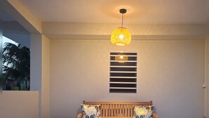 Um banco de madeira com assento e encosto de ripas, acompanhado de uma mesa de madeira combinando. Uma luminária pendente está suspensa do teto.