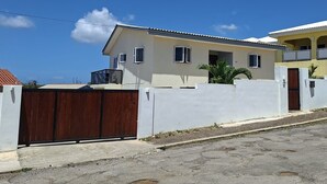 Um edifício residencial de dois andares com fachada branca, um portão marrom e céu azul claro.