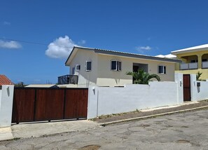 Ein zweistöckiges Wohngebäude mit weißer Fassade, einem braunen Tor und blauem Himmel.