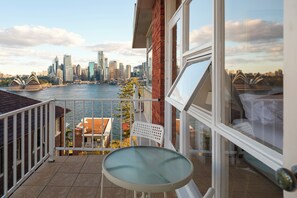 Ein Balkon mit Tisch und Stühlen, mit Blick auf eine Skyline, in der sich ein Fluss und markante Gebäude spiegeln.