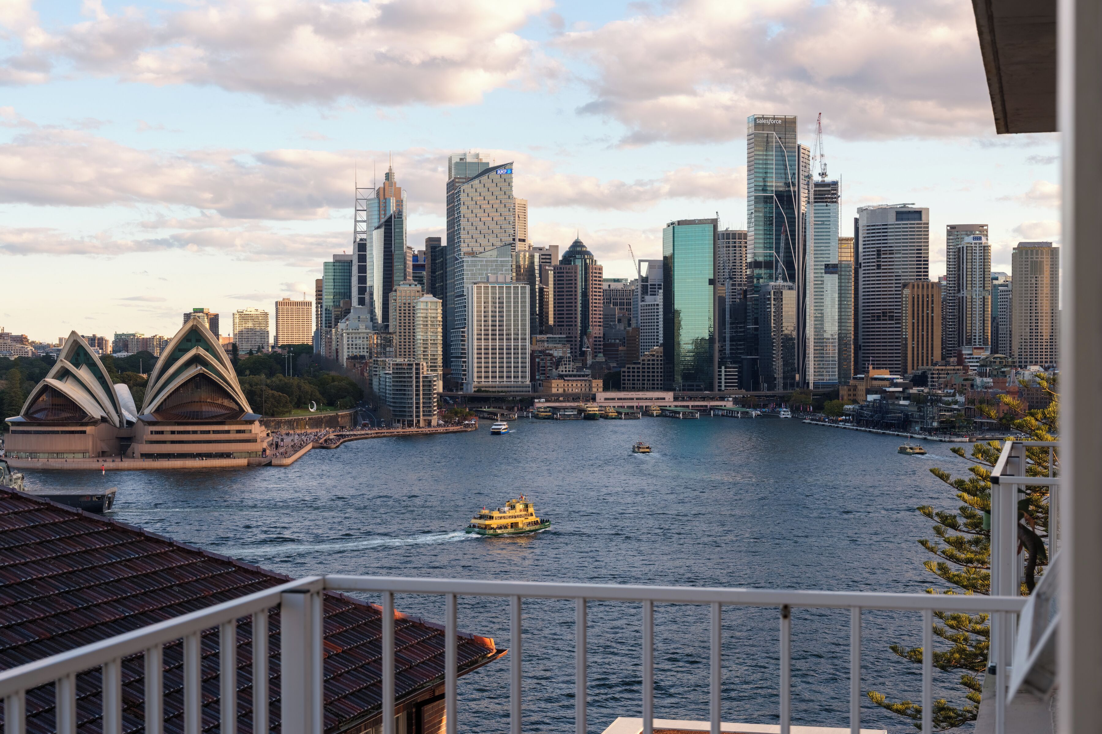 A city skyline with modern buildings, a harbor with boats, and the Sydney Opera House in the foreground.