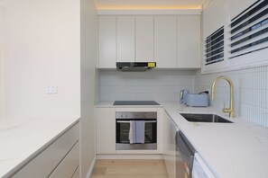 Eine kleine Küche mit weißen Schränken, einem eingebauten Ofen, einer Spüle mit goldfarbenem Wasserhahn und einem Toaster.