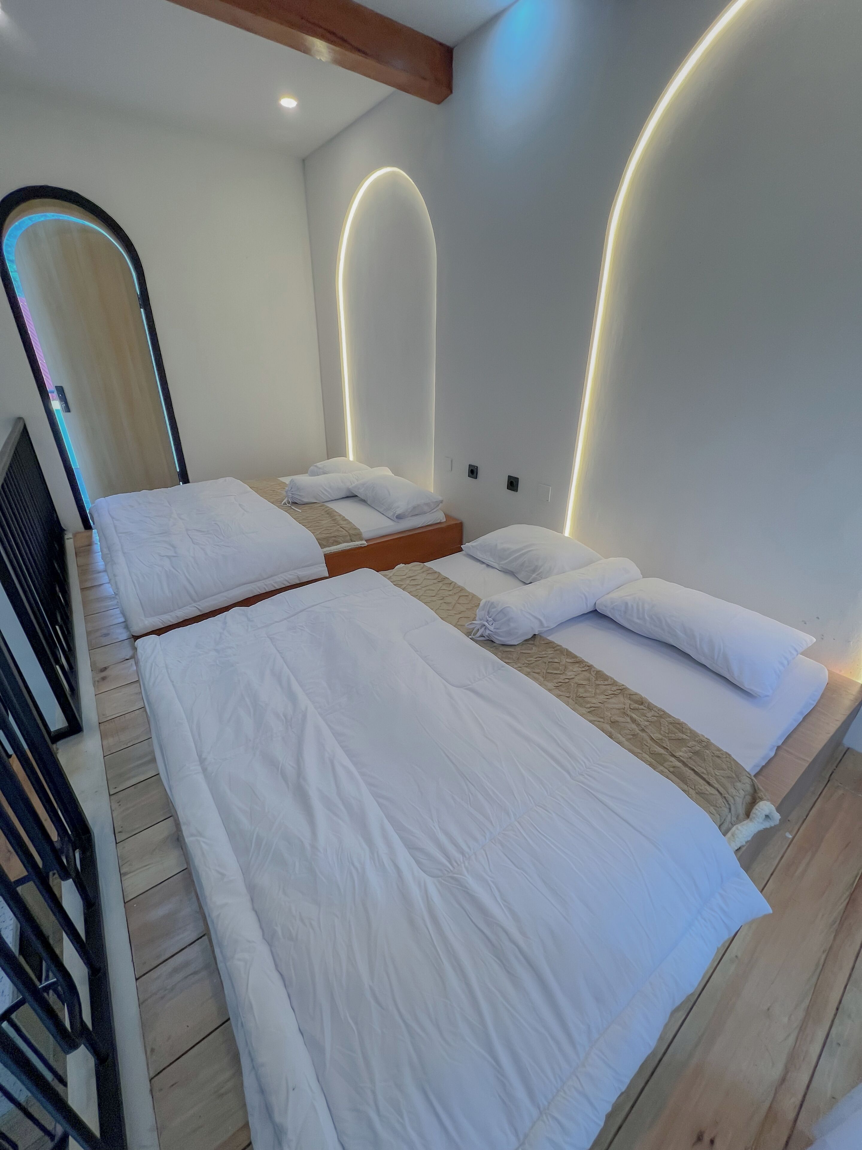 A hotel room with two beds, wooden flooring, and modern wall lighting.