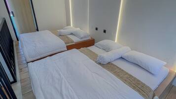 A hotel room with two beds, wooden flooring, and modern wall lighting.