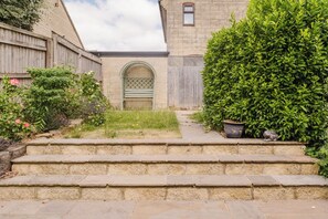 A stone staircase leading to a gated entrance with a green archway, surrounded by lush greenery and a wooden fence.