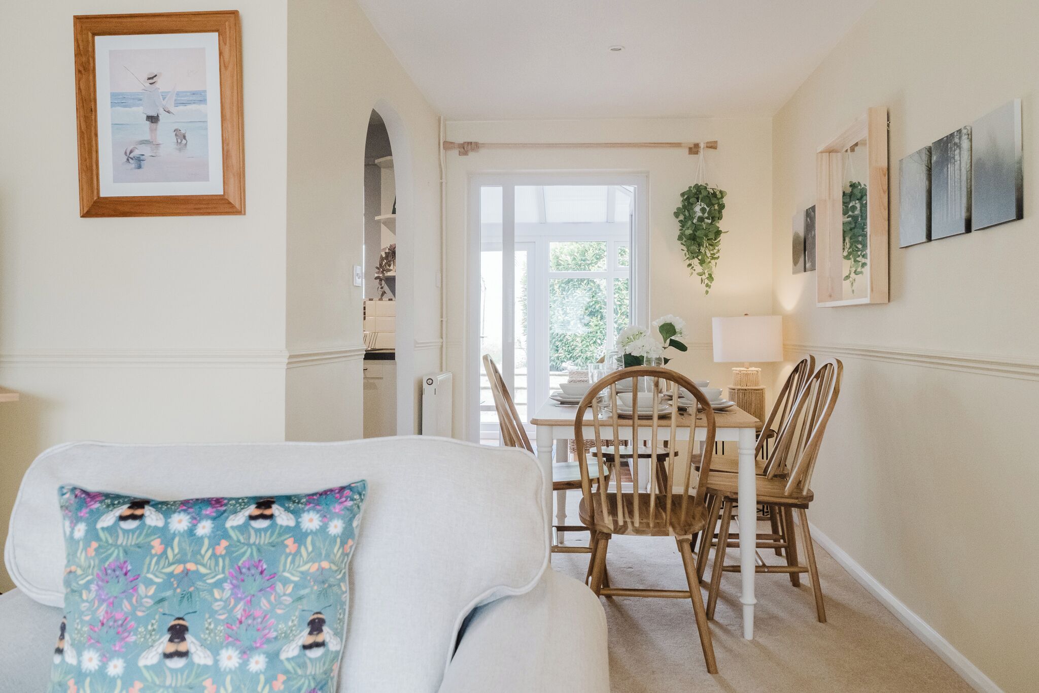 A cozy dining area with a table set for four, a white sofa with a floral pillow, and a framed picture on the wall.