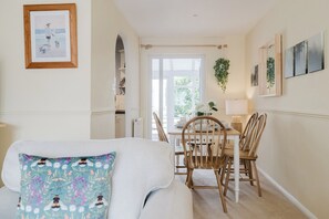 A cozy dining area with a table set for four, a white sofa with a floral pillow, and a framed picture on the wall.