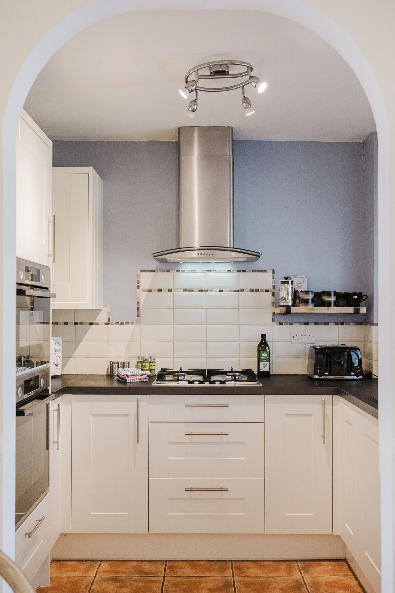 A modern kitchen with white cabinets, a stainless steel range hood, and a tiled backsplash.